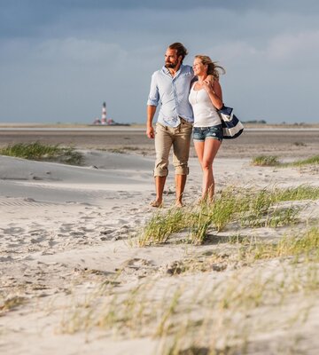 Spaziergang eines Paares am Strand mit dem Westerhever Leuchtturm im Hintergrund