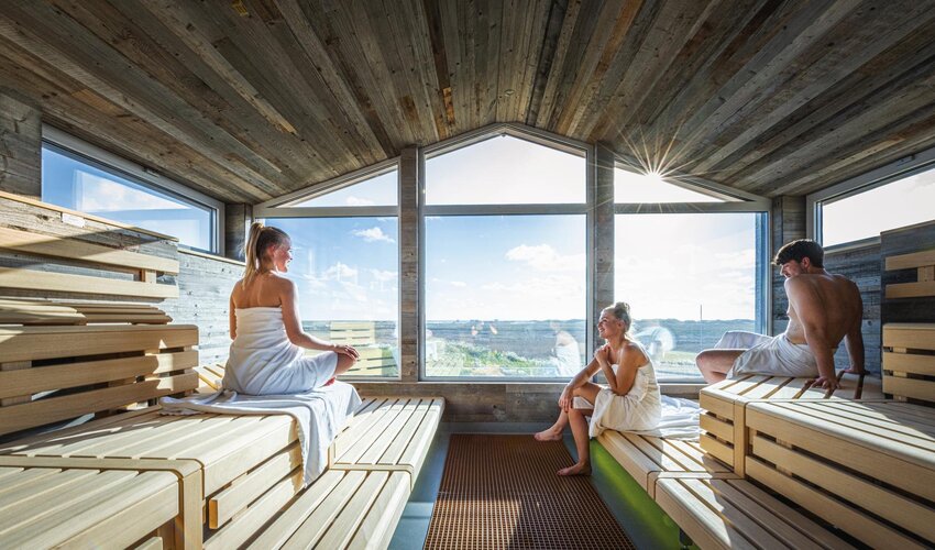Zwei Damen und ein Man in der Pfahlbausaune mit Ausblick auf das Meer 