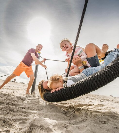 Familie beim Toben auf dem Strandspielplatz mit Nestschaukel