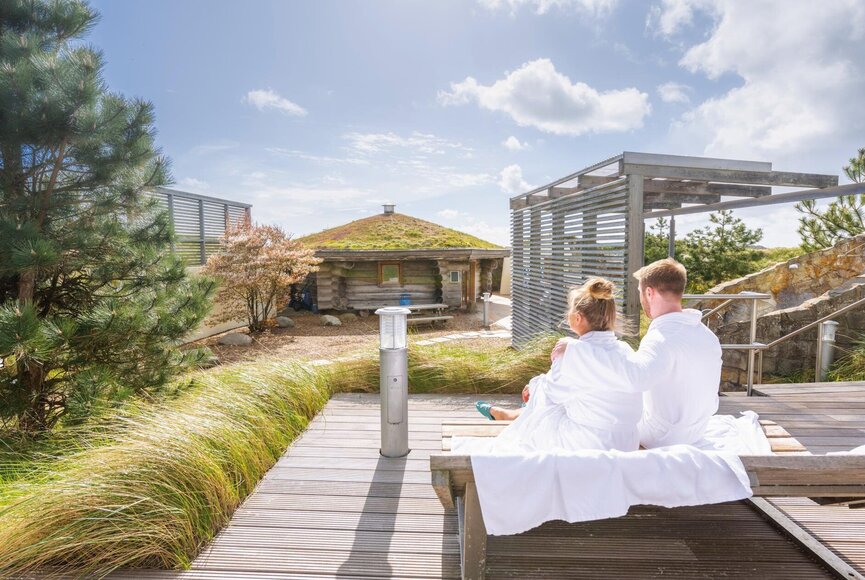 Paar entspannt auf Doppelliege im Dünengarten des Saunabereichs