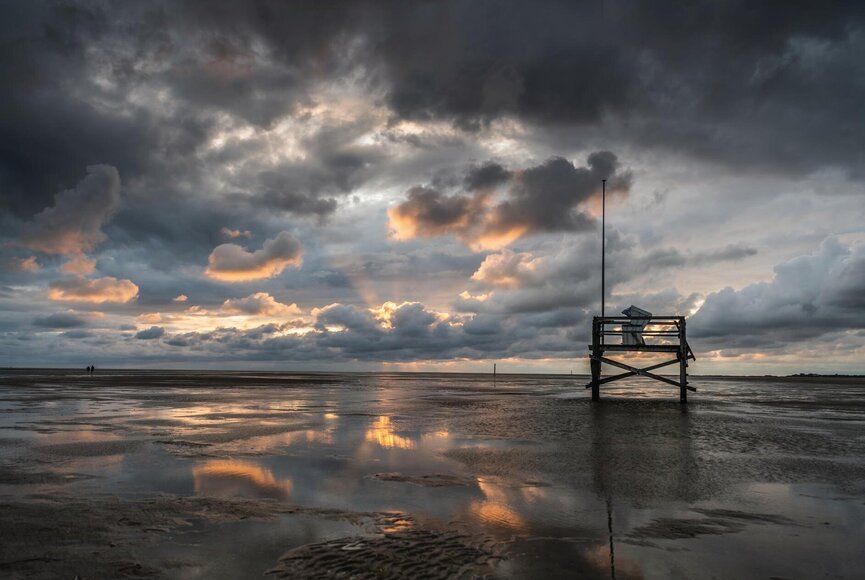 Holzpodest mit einem Strandkorb darauf beim Sonnenuntergang am Strand mit Wolken