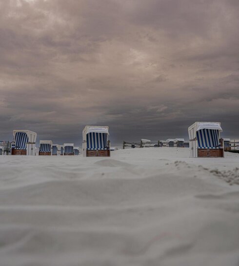 Strandkörbe im Sand bei dunklen, rosa Wolken