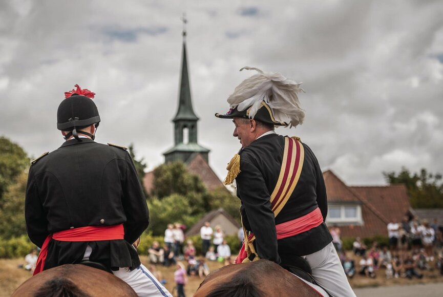Reiter mit festlicher Kleidung und Pferden auf dem Marktplatz im Dorf