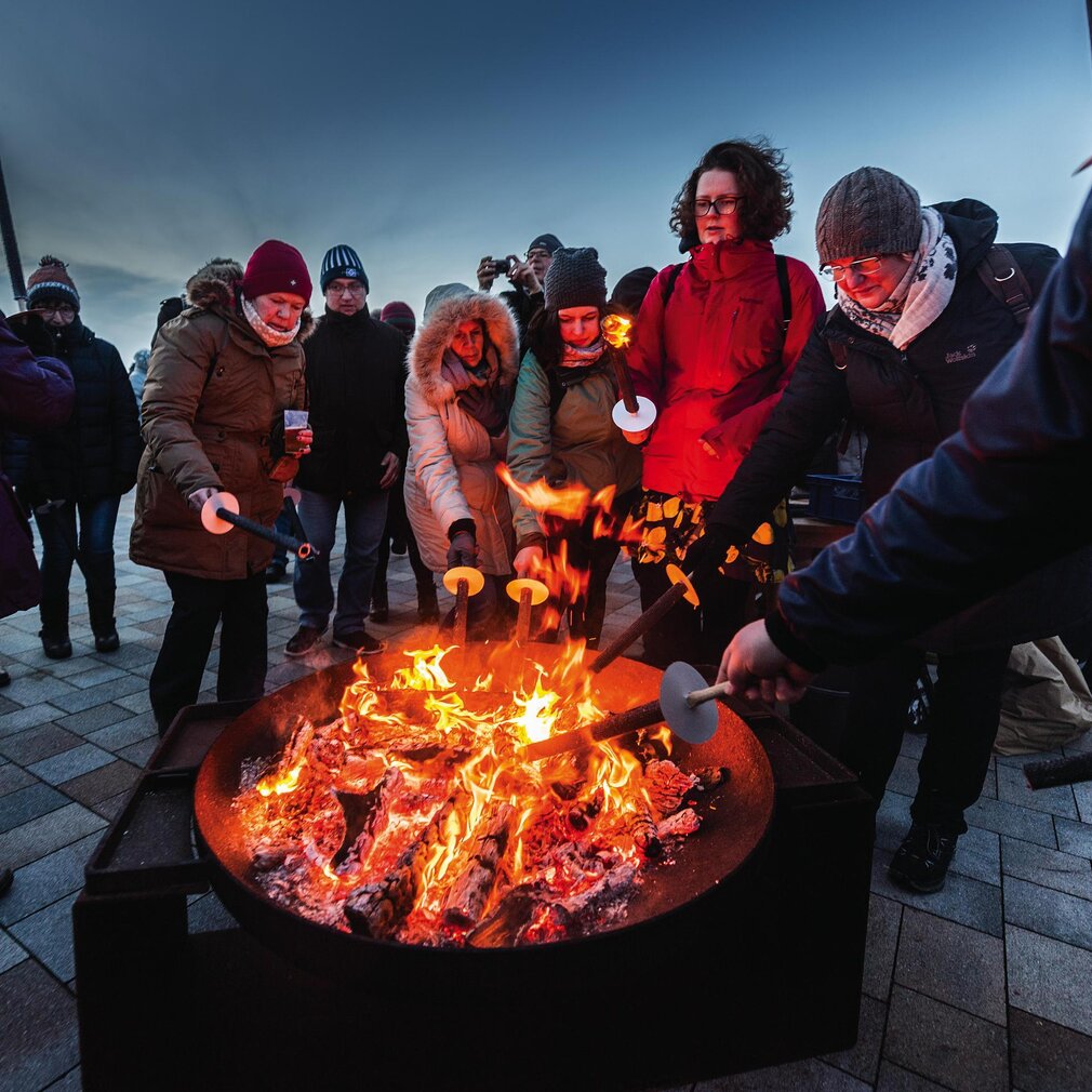 Personen stehen um eine Feuerschale und zünden Fackeln an